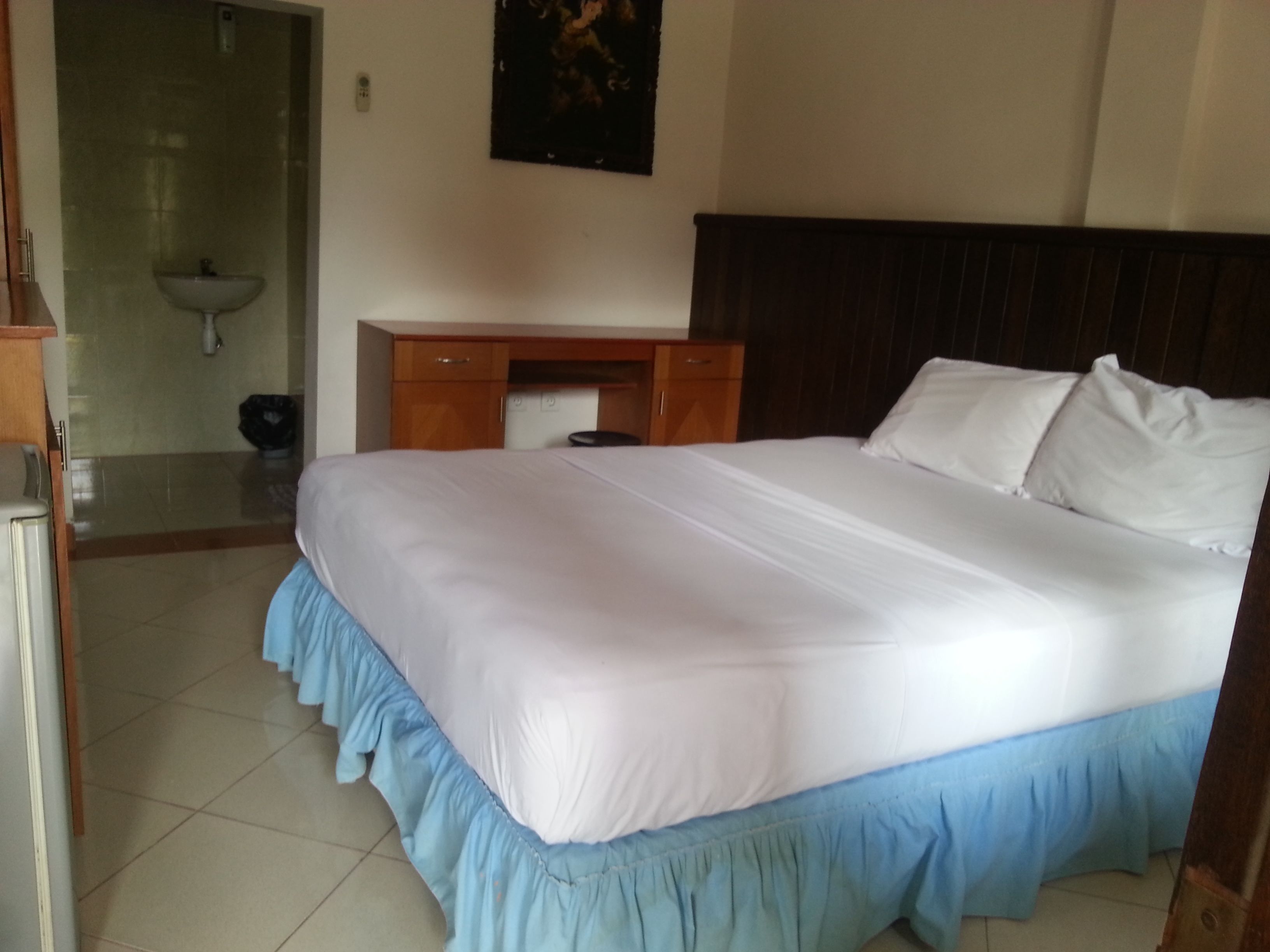 Een hotelkamer met een groot bed, een houten bureau en een badkamer met een wastafel.