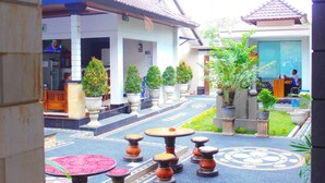 A courtyard with potted plants, a tiled floor, and a traditional building with a tiled roof. - New Asta Graha Homestay (Kedonganan)