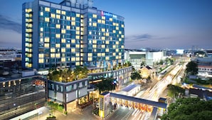 Un hotel moderno con fachada de vidrio, varios pisos y un jardín en la azotea.
