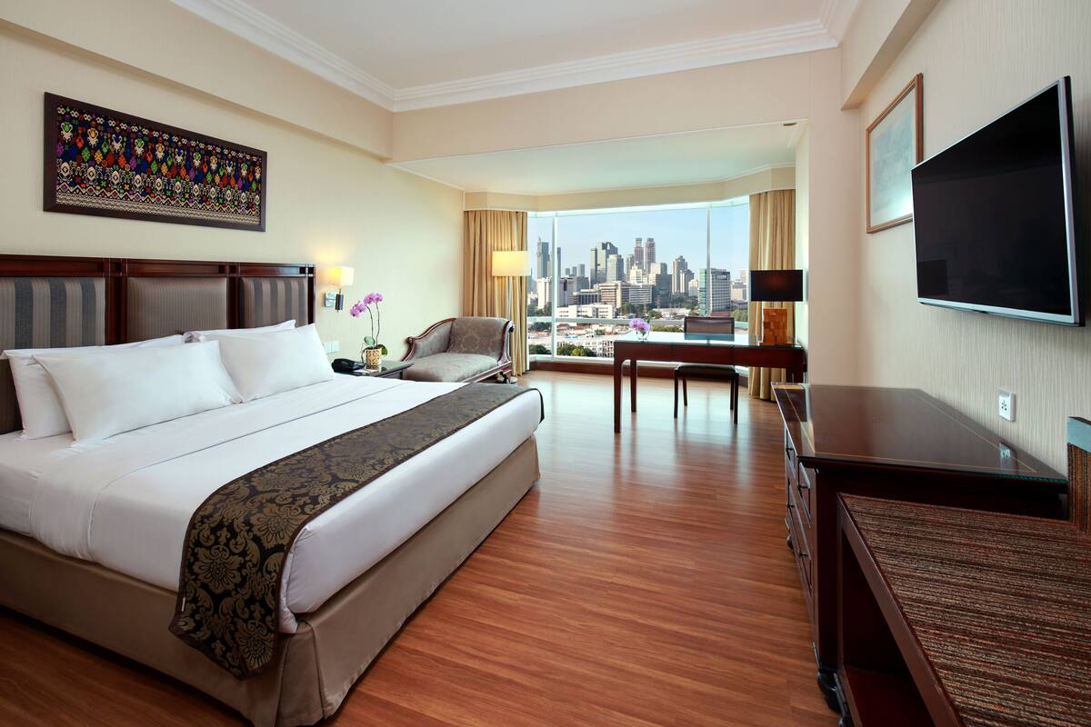 A hotel room with a large bed, a desk, a chair, a TV, and a city view.