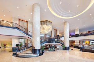 Un'ampia hall con un'imponente scalinata, grandi colonne e un moderno lampadario.