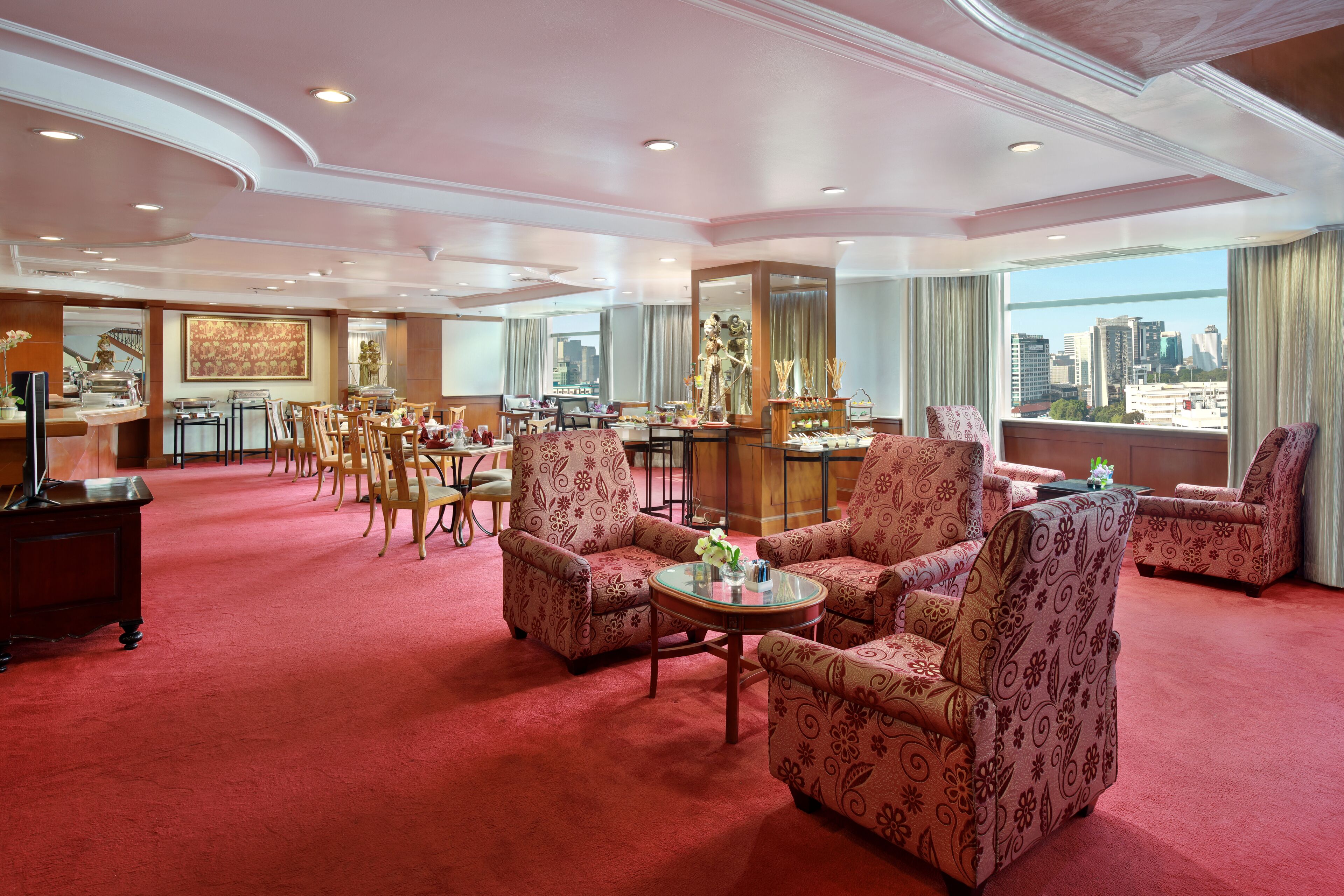 Un vestíbulo de hotel espacioso con sillones estampados, una mesa de centro y una zona de comedor con mesas y sillas.