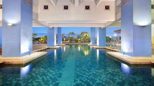 Una amplia piscina interior con agua cristalina azul, rodeada de pilares azules y un suelo de baldosas.