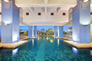 Un'ampia piscina interna con acqua cristallina e blu, circondata da pilastri blu e pavimento piastrellato.