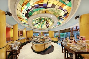 Una hall d'albergo con un buffet centrale, ampie finestre e un soffitto in vetro colorato.