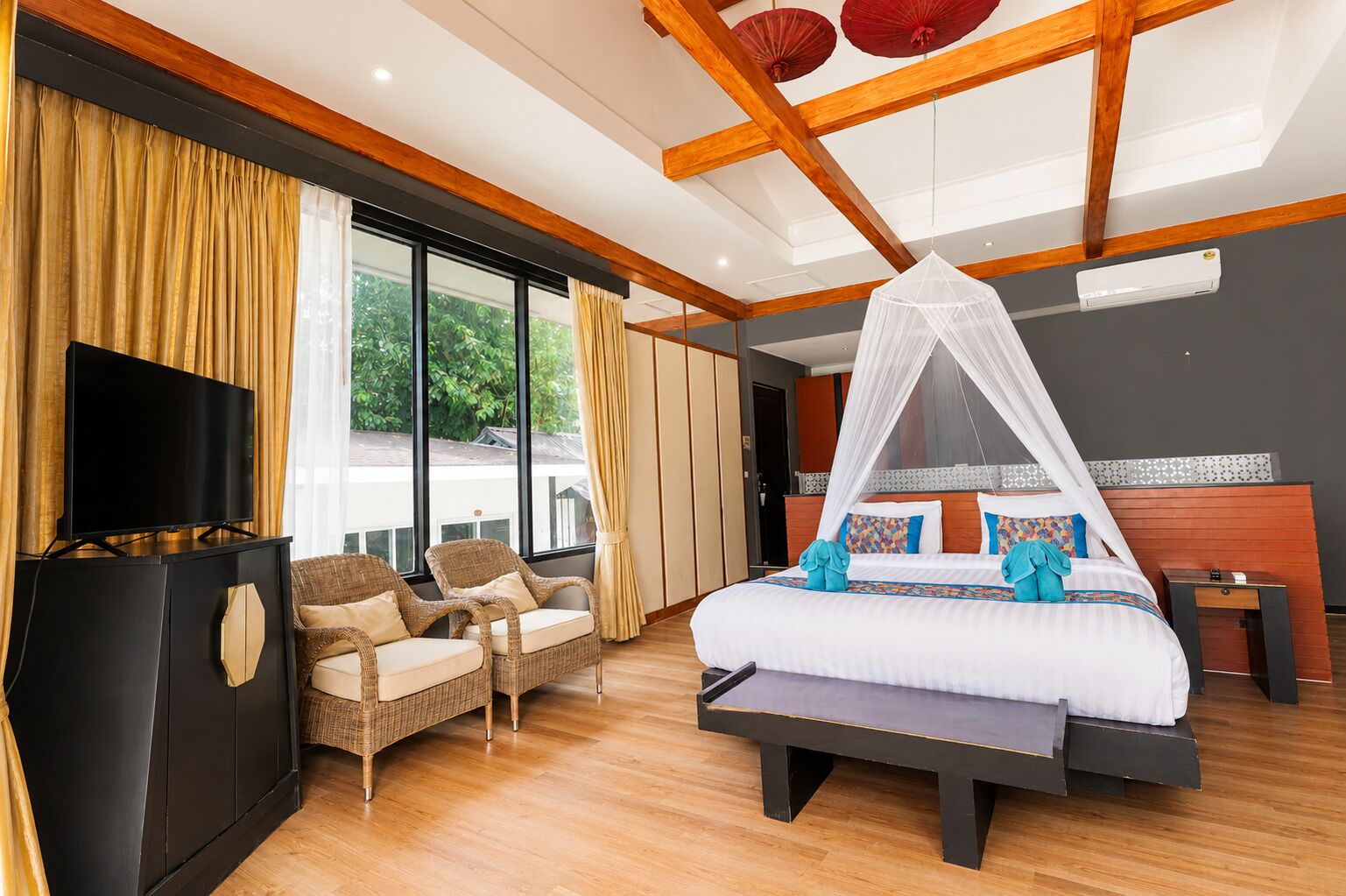 A modern hotel room with a large bed, a TV, wicker chairs, and a balcony with curtains.