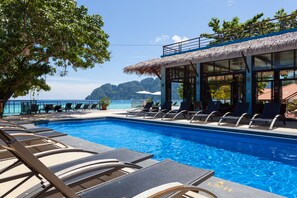 A swimming pool with lounge chairs, a thatched-roof building, and a view of the ocean. - Phi Phi Long Beach Resort & Villa (Ko Phi Phi)