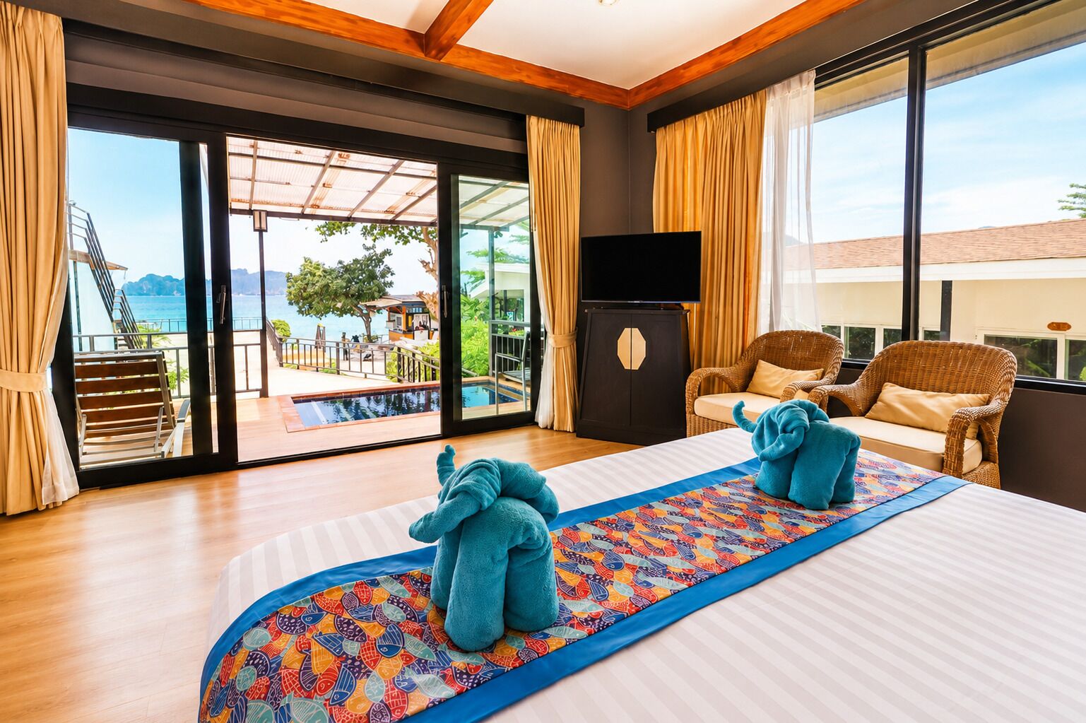 A hotel room with a bed, a television, a sofa, and a view of a pool and mountains.
