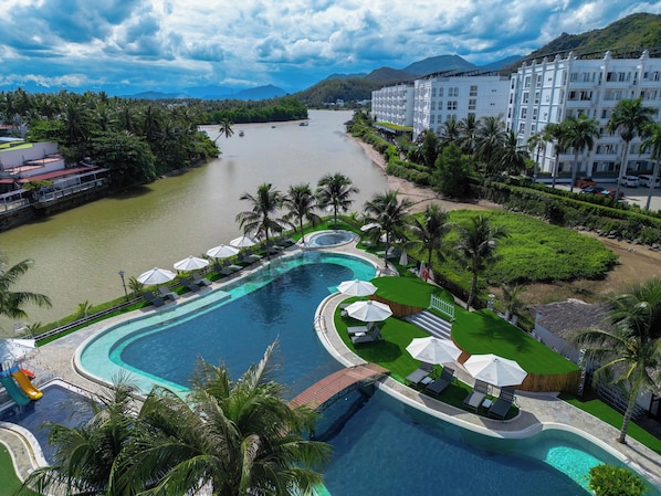 A resort with a large swimming pool, palm trees, and a view of a river and mountains. - Champa Island Nha Trang - Resort Hotel & Spa (Nha Trang)