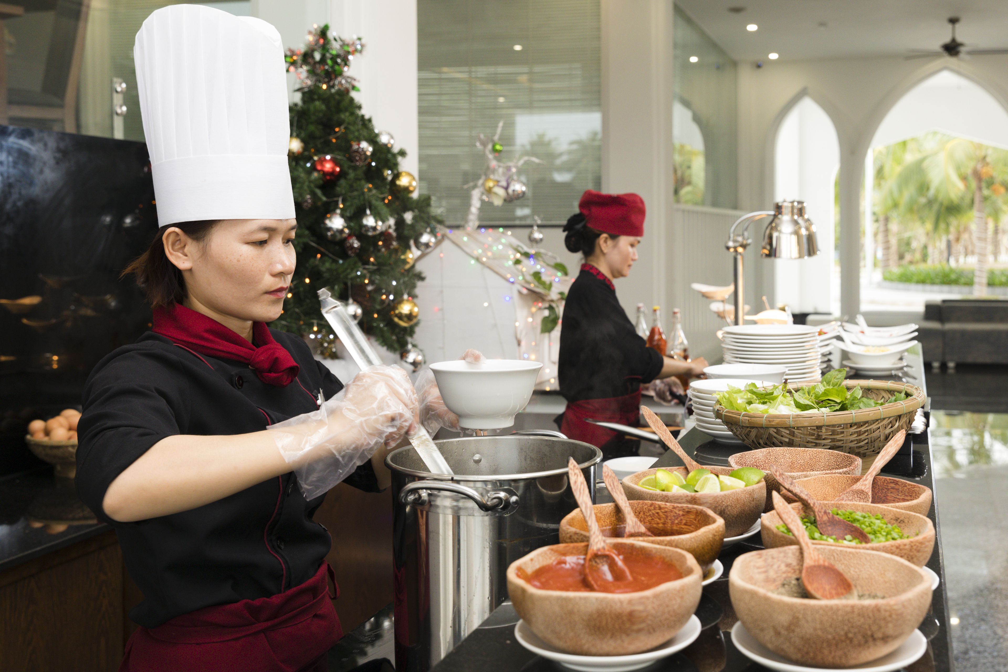 A buffet setup with various food containers and a Christmas tree in the background.