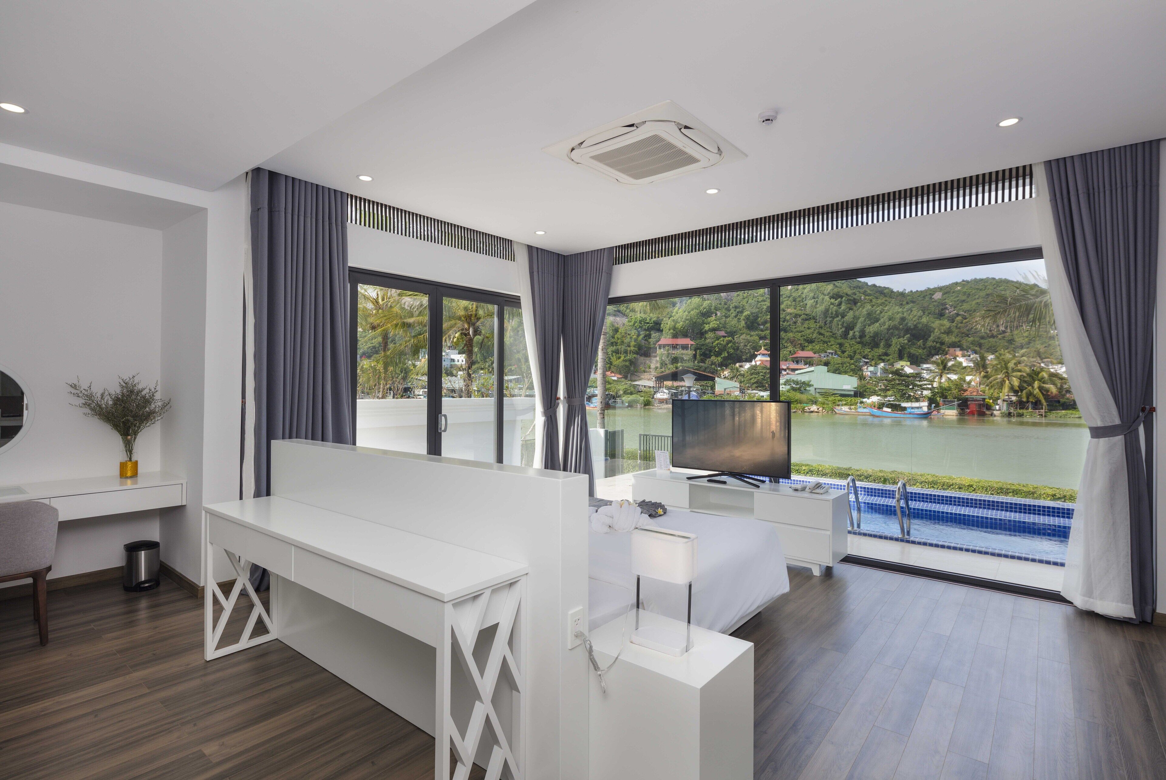 Ein modernes Hotelzimmer mit großem Fenster, Schreibtisch, Bett und Fernseher.
