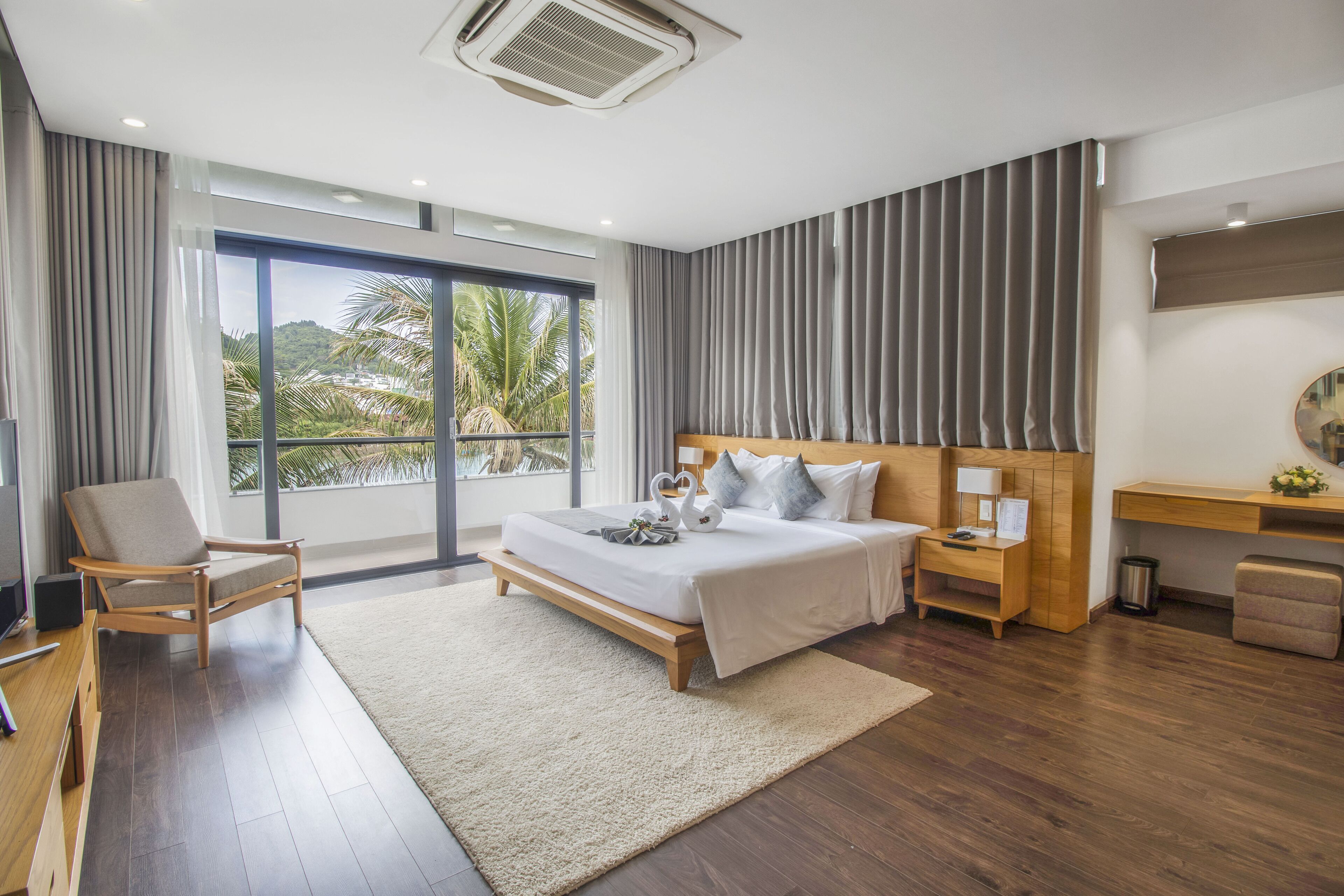 A modern hotel room with a large bed, a desk, a chair, and a view of palm trees.