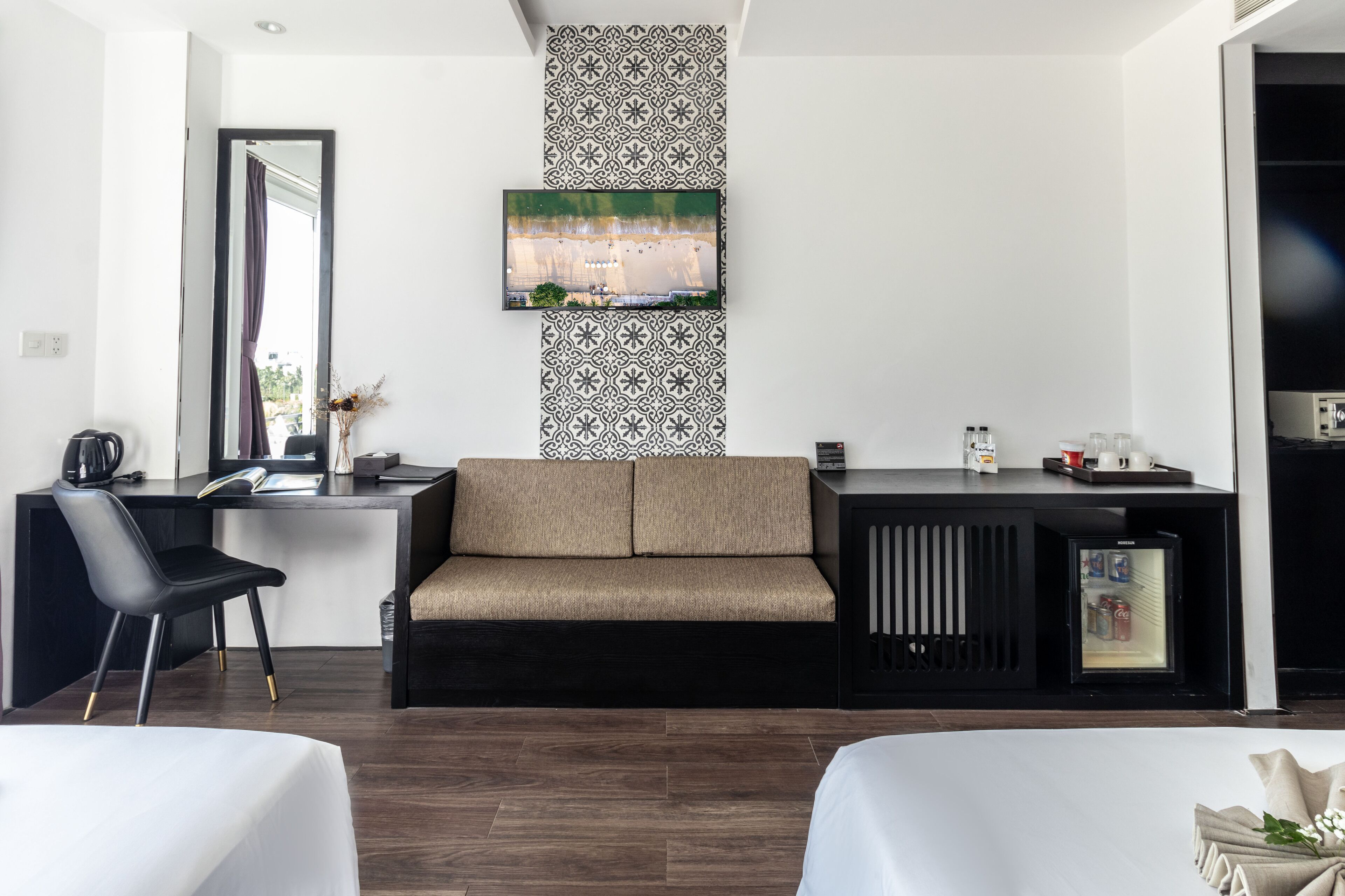 Een moderne hotelkamer met een bank, bureau, koffiezetapparaat, koelkast en een aan de muur bevestigde televisie.