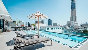 A rooftop pool with lounge chairs and an umbrella, overlooking a cityscape with modern buildings. - Vince Hotel Pratunam (Bangkok)