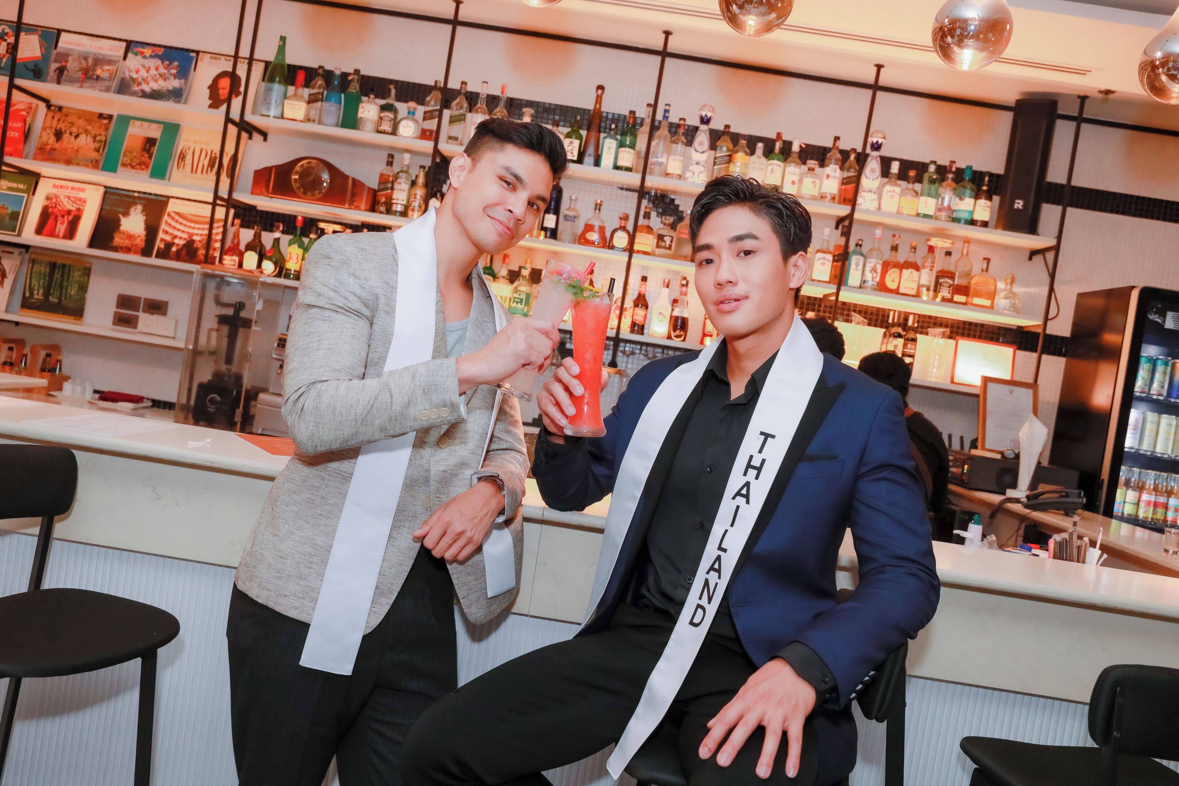 Dos hombres en un bar, con estantes llenos de botellas de licor al fondo.