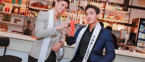 Dos hombres en un bar, con estantes llenos de botellas de licor al fondo.