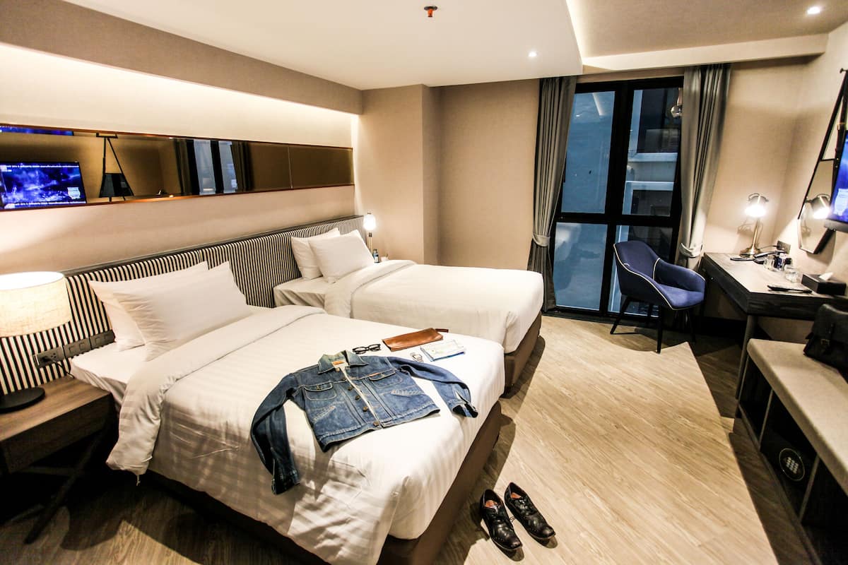 Une chambre d’hôtel avec deux lits, un bureau, une chaise et un téléviseur fixé au mur.