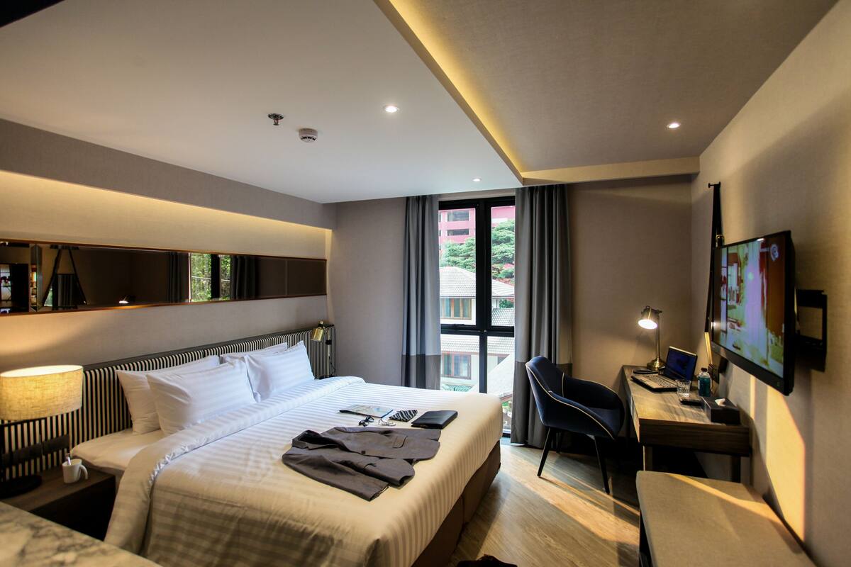Une chambre d’hôtel avec un grand lit, un bureau avec un ordinateur, une chaise et un téléviseur fixé au mur.