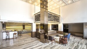 A spacious lobby with a high ceiling, a central column, and a seating area with a sofa and chairs. - Vince Hotel Pratunam (Bangkok)