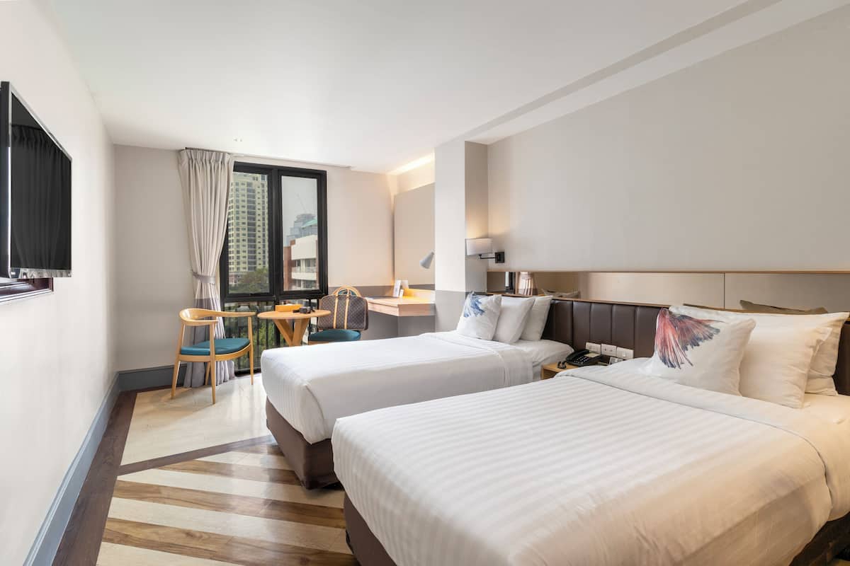Une chambre d’hôtel avec deux lits, un bureau, une chaise et une fenêtre avec des rideaux.