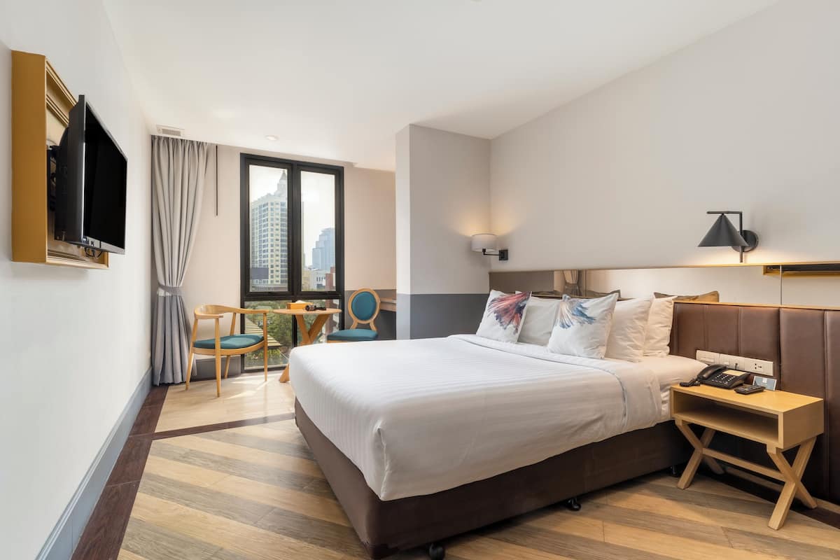 Une chambre d’hôtel avec un grand lit, un téléviseur fixé au mur, un bureau avec un téléphone et une chaise.