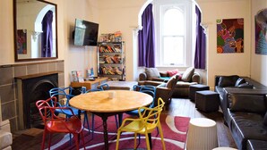 A living room with a fireplace, a round table with chairs, a sofa, a television, and a bookshelf. - Original Backpackers (Potts Point)
