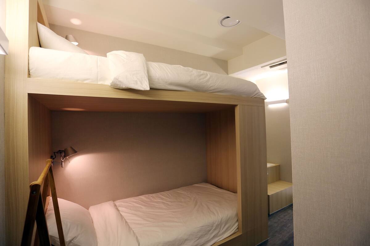 A bunk bed with a wooden frame, a bedside table, and a lamp.