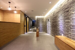 A modern reception area with a wooden reception desk, a bench, and a brick wall. - Hotel 8 Hours (Seoul)