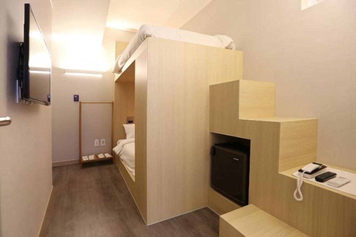 A compact hotel room with a bunk bed, a desk with a telephone, and a television mounted on the wall.
