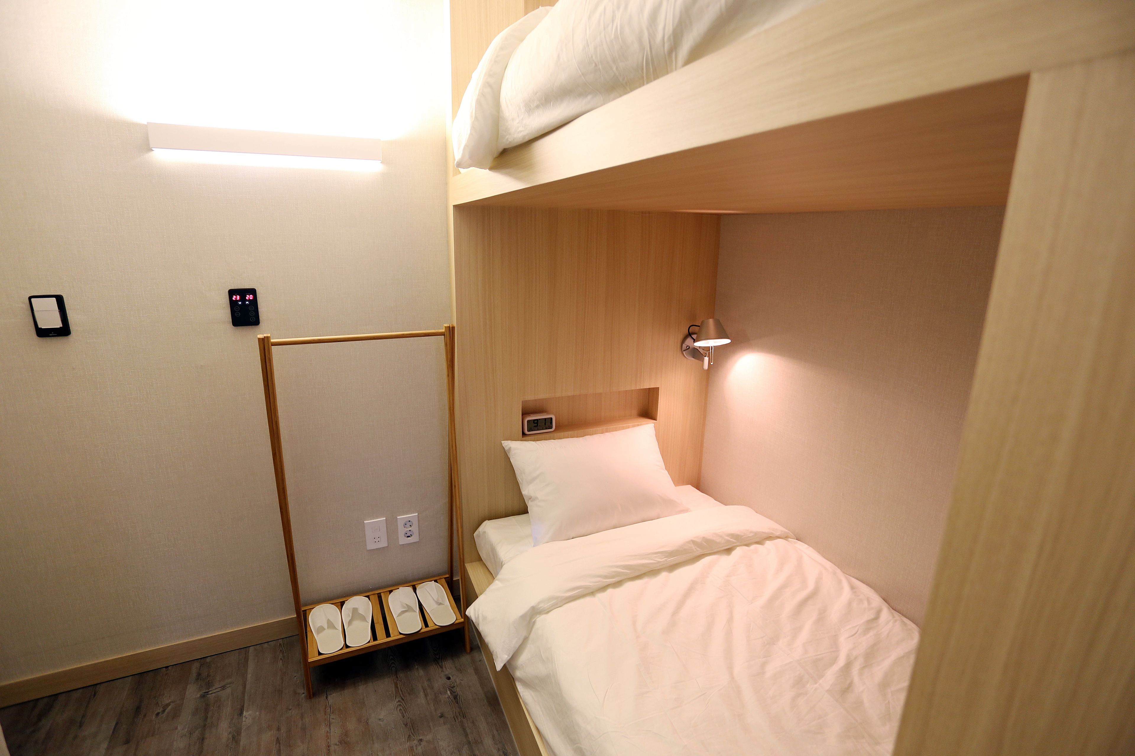 A bunk bed room with a wooden headboard, a bedside table with a lamp, and a shoe rack.