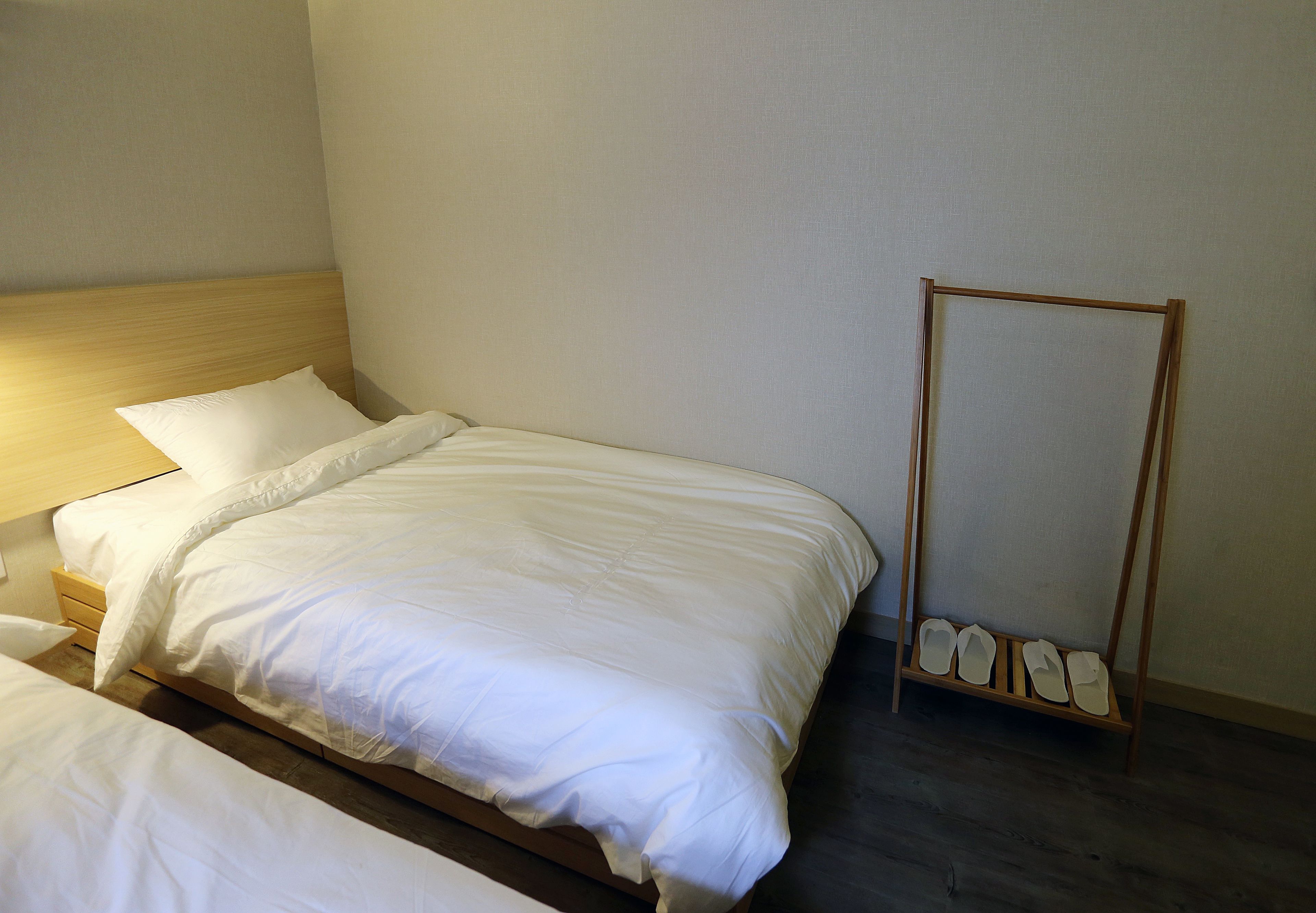 Uma cama de solteiro com cabeceira de madeira, uma mesinha de cabeceira e um sapateiro.
