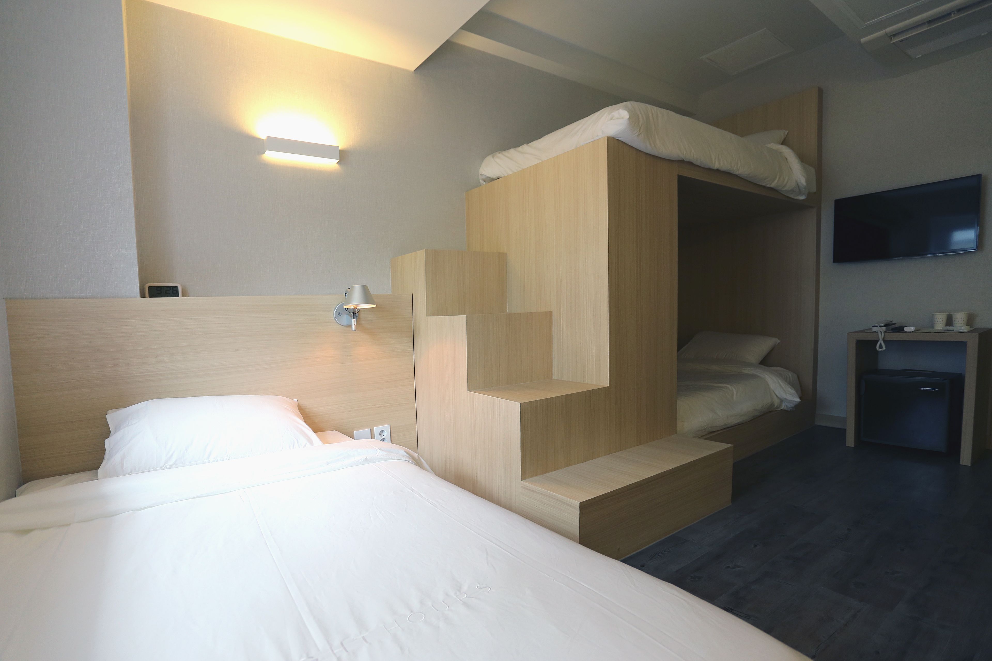 Una habitación de hotel moderna con una cama litera, un televisor de pantalla plana en la pared y un escritorio pequeño con una lámpara.