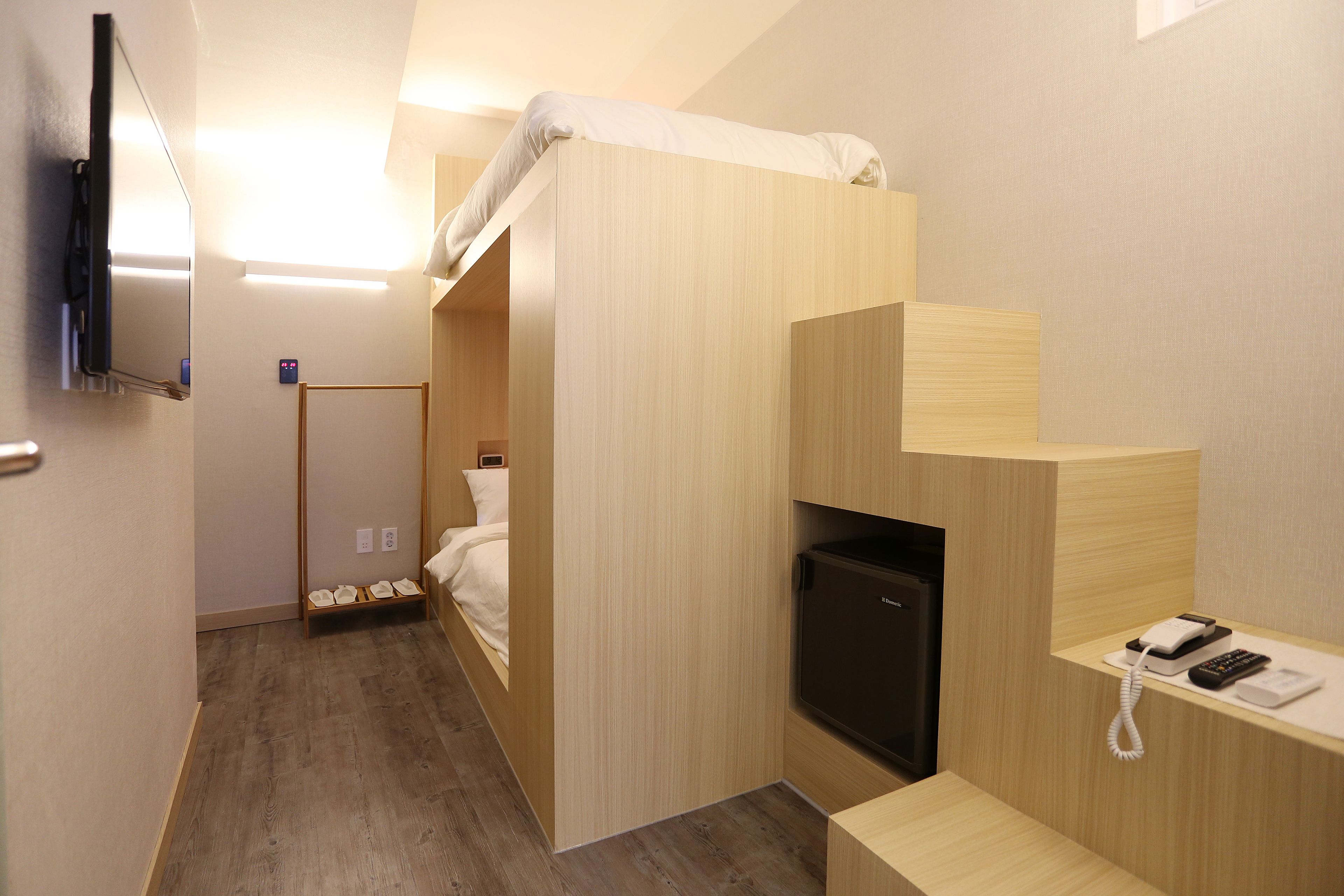 A compact hotel room with a bunk bed, a small desk with a telephone, and a television mounted on the wall.