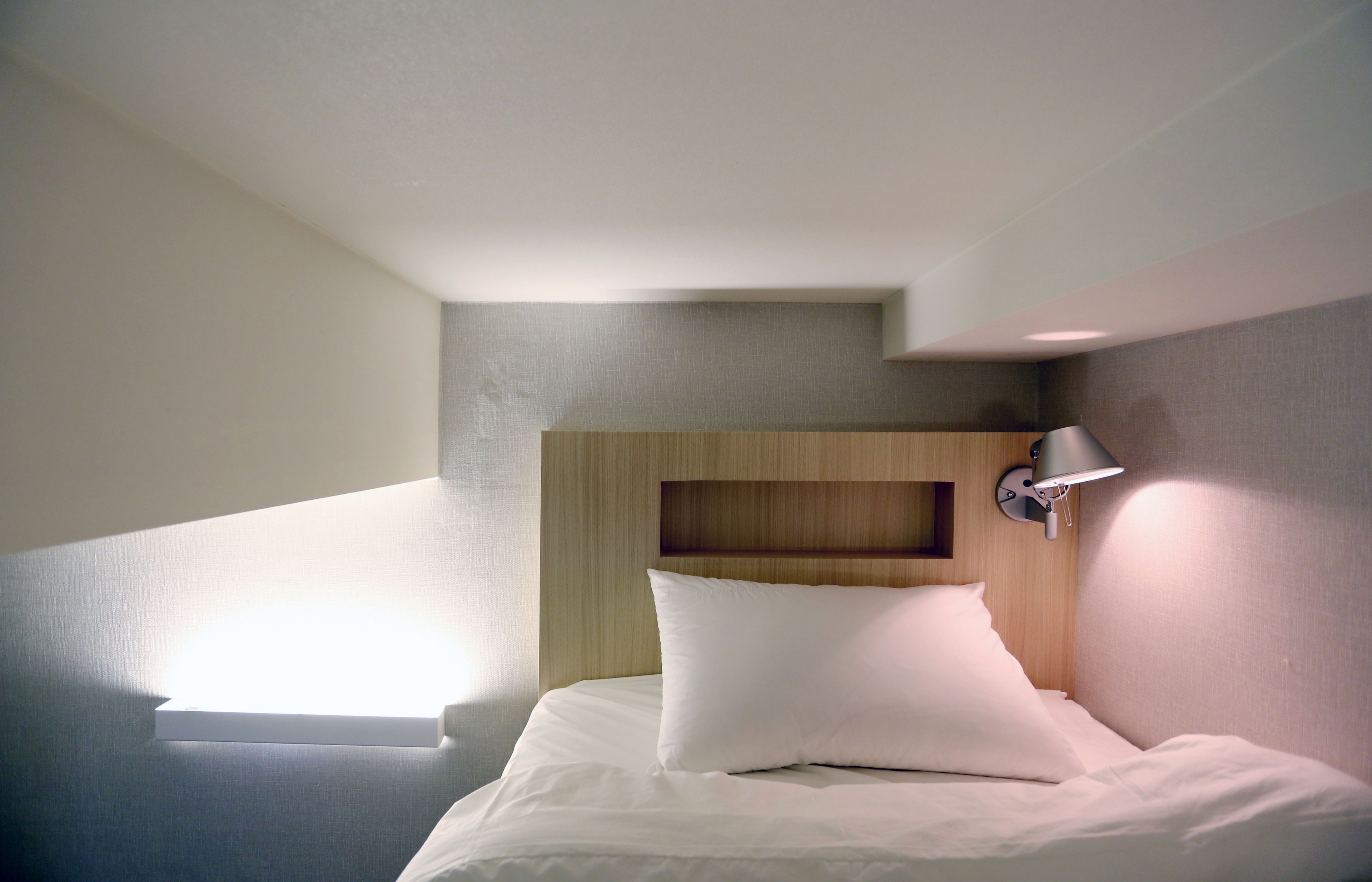 Een moderne hotelkamer met een bed, een wandlamp en een schuin dak.