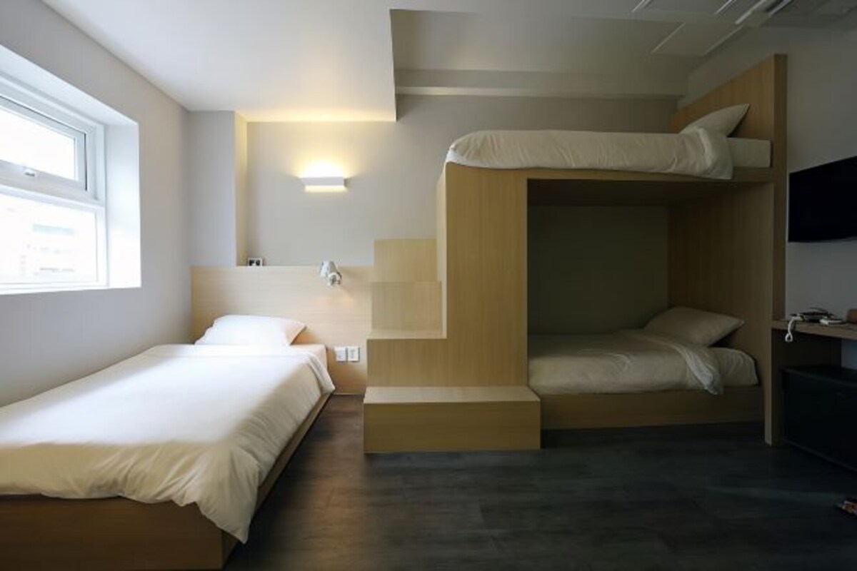 A modern hotel room with a bunk bed, a single bed, and a desk with a chair.