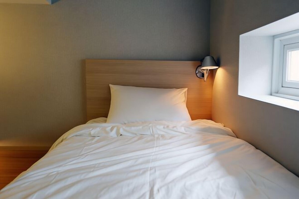 A neatly made bed with a wooden headboard and a wall-mounted light fixture.