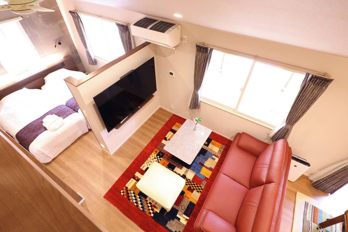 Un espacio habitable pequeño con un sofá, un televisor, un tapete estampado y una mesita.