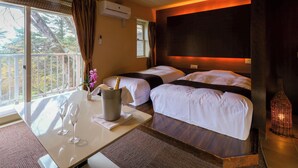 Une chambre d’hôtel avec deux lits, une table à manger avec deux verres à vin, un vase de fleurs et une vue sur les arbres par la fenêtre.