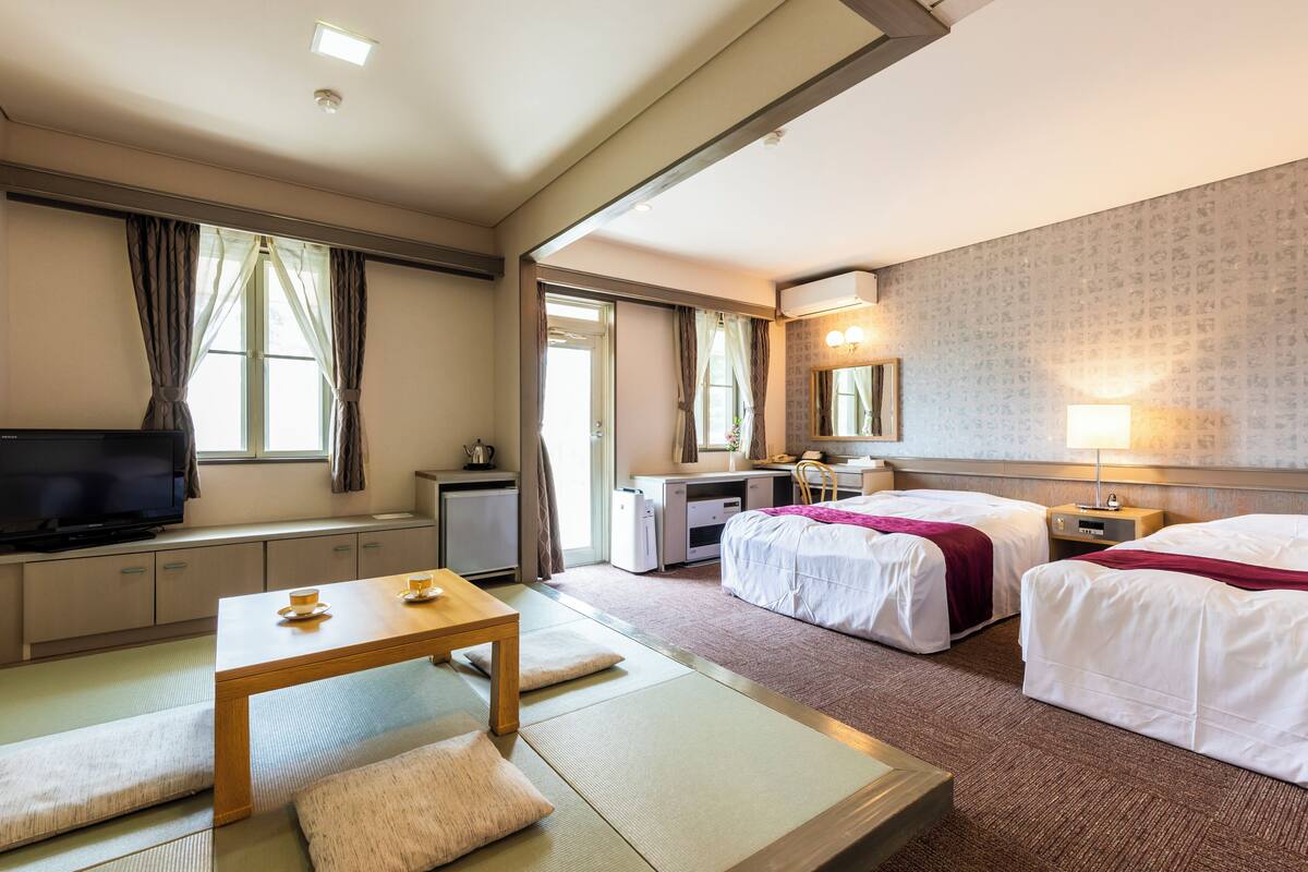 Een hotelkamer met twee bedden, een bureau, een televisie en een zithoek met tatami matten.