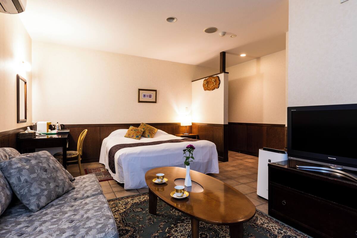Een hotelkamer met een bed, een slaapbank, een salontafel, een televisie en een bureau met een lamp.
