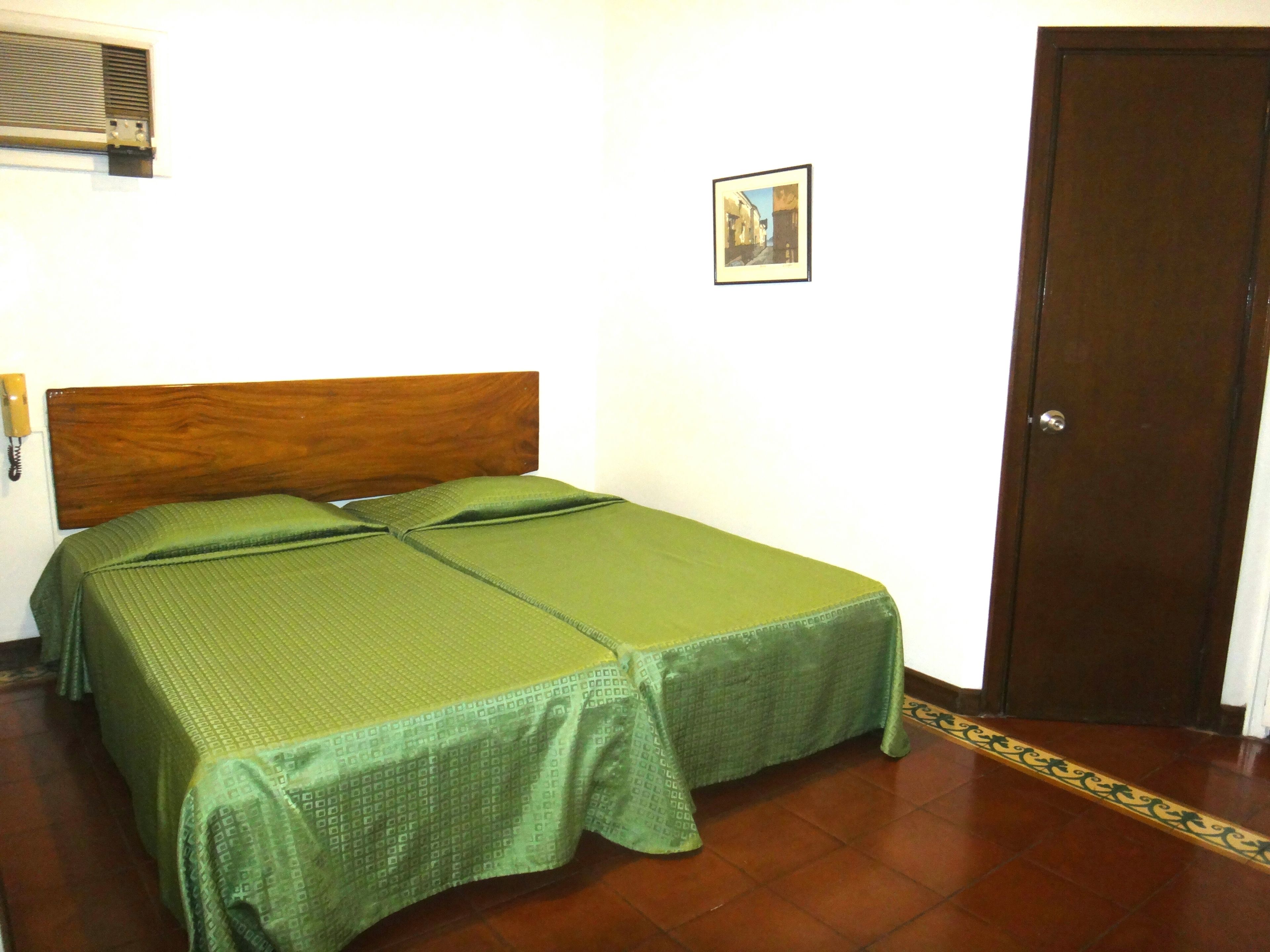Een enkel bed met een houten hoofdbord, een groene dekbedovertrek en een klein ingelijst beeld aan de muur.