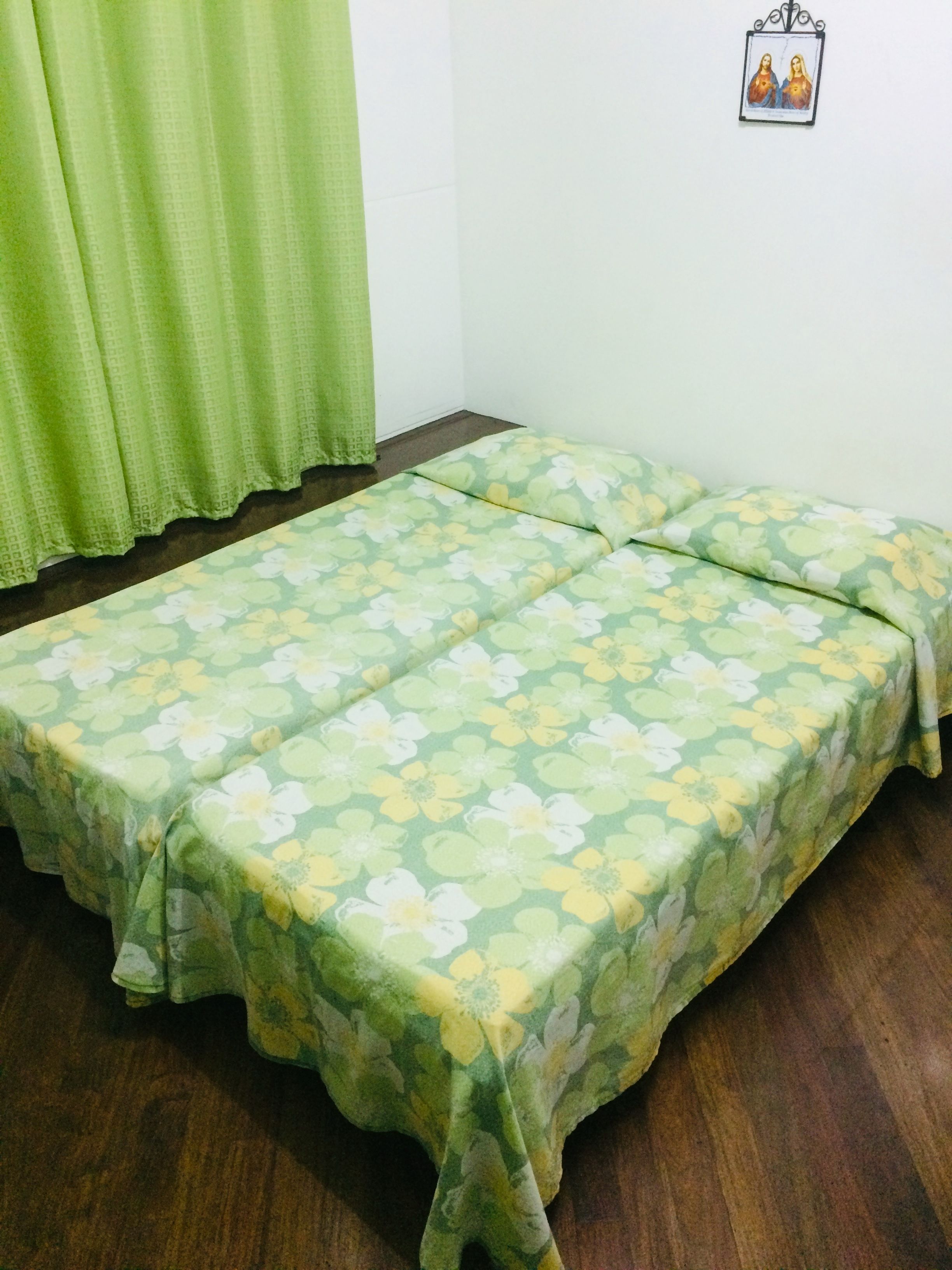 Una habitación con una cama cubierta con ropa de cama de estampado floral, piso de madera y una cortina verde.