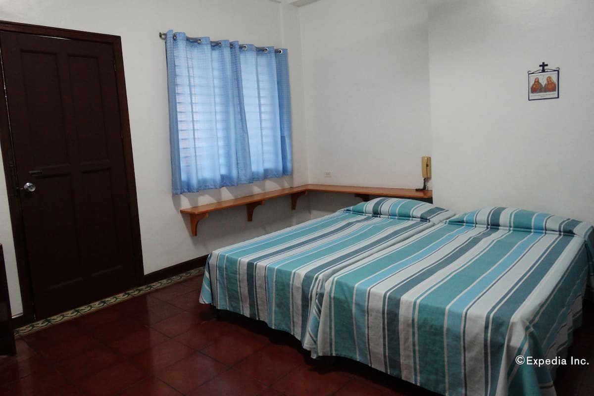 A room with a bed, a wooden bench, a door, and a window with curtains.