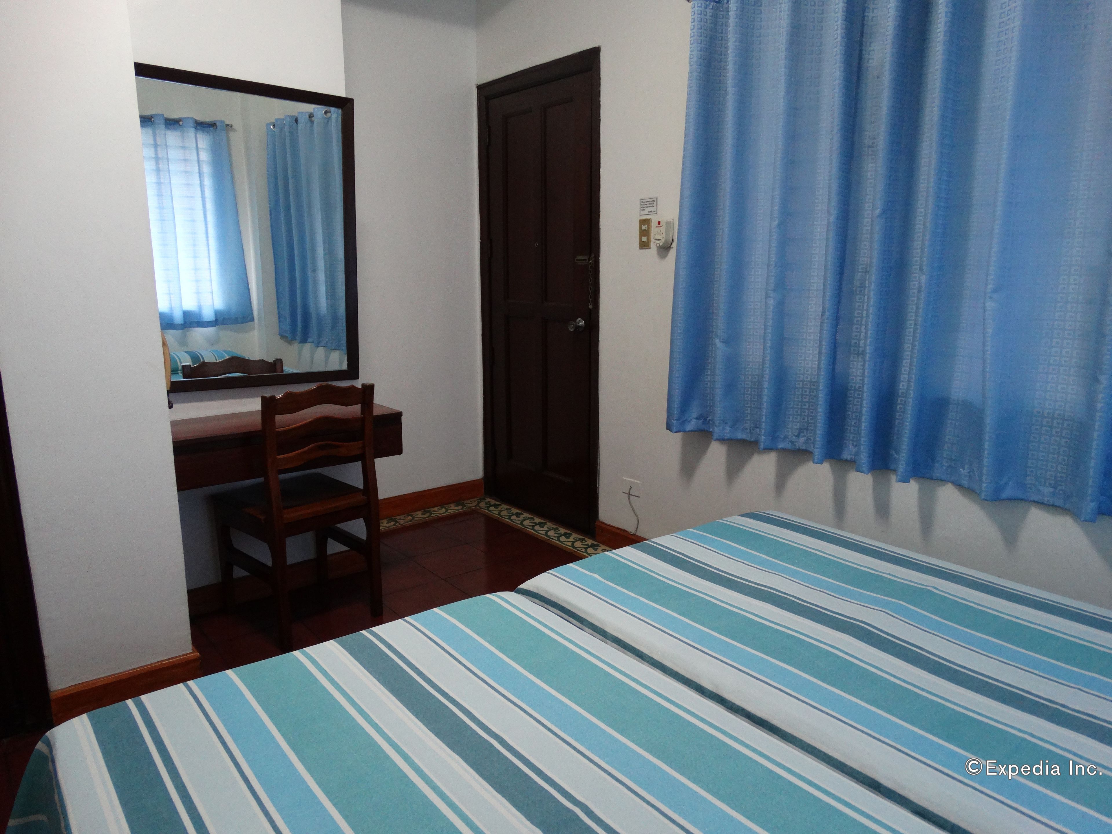 A room with a bed, a desk, a chair, a mirror, a door, and a window with curtains.