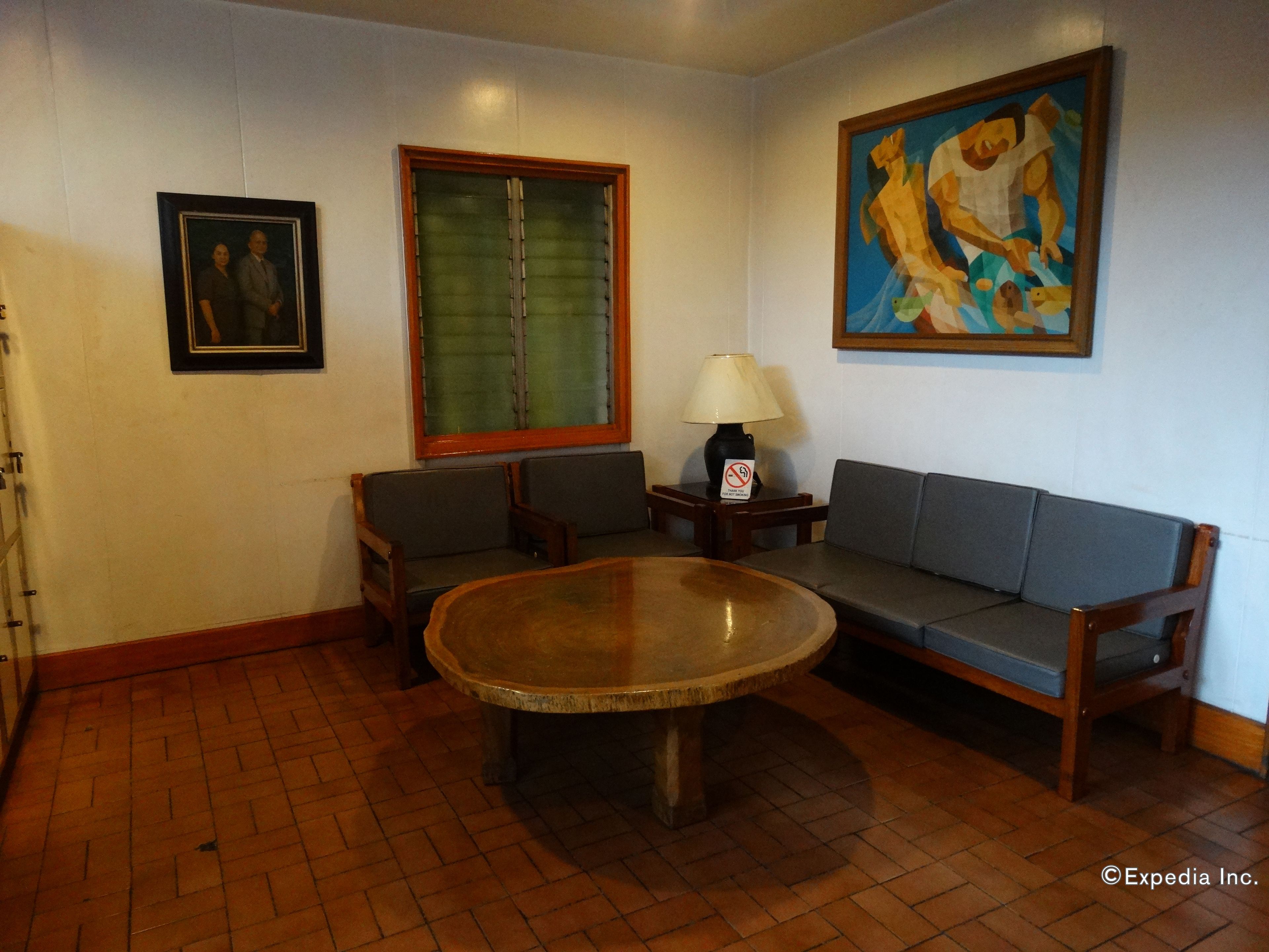 A room with a round table, two sofas, a painting, and a window with blinds.
