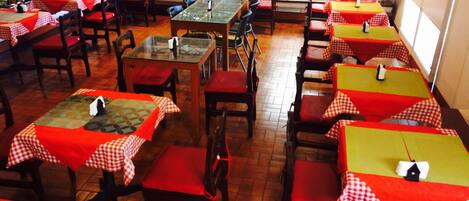A restaurant with tables covered in red and yellow checkered tablecloths, wooden chairs, and a tiled floor.
