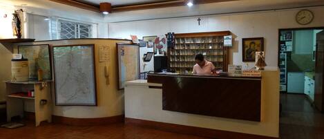 A reception area with a wooden reception desk, a map on the wall, a clock, and a cross.