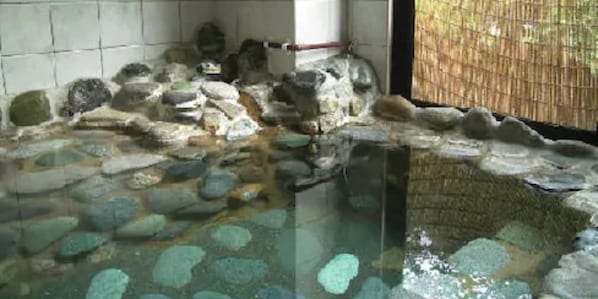 Un área de baño con bañera de piedra, separador de bambú, repisa de piedra y estructura de madera.