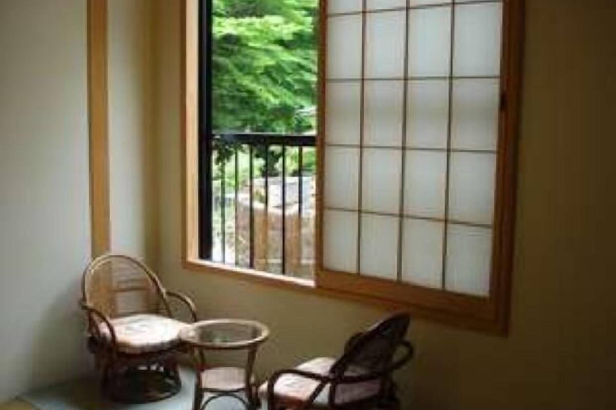 A room with a tatami mat floor, a sliding door with a grid pattern, and two traditional Japanese chairs.