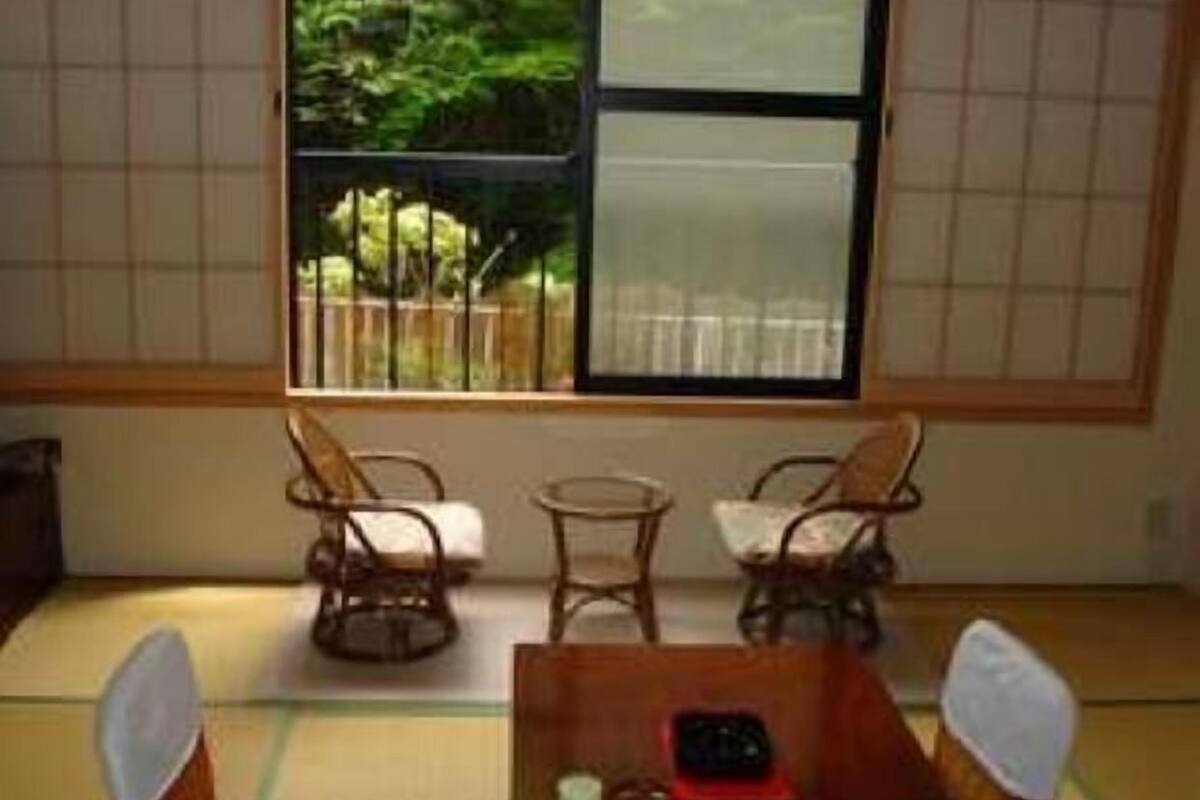 A traditional Japanese room with tatami flooring, a low table with a tea set, and a view of a garden through a sliding door.